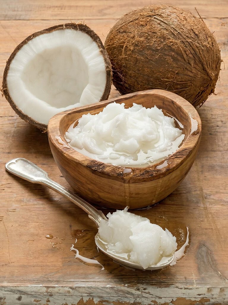 Fresh organic coconut oil in a wooden bowl with coconut and spoon on rustic wood.